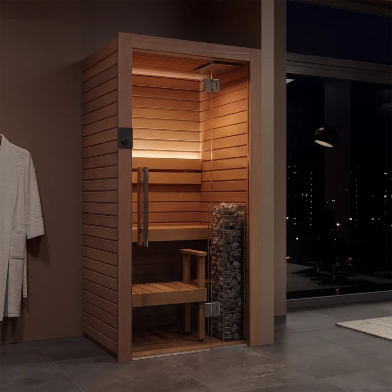 Wood-paneled sauna with glass door, bench, and a heater rock display; robe hangs nearby, city lights visible through the window at night.