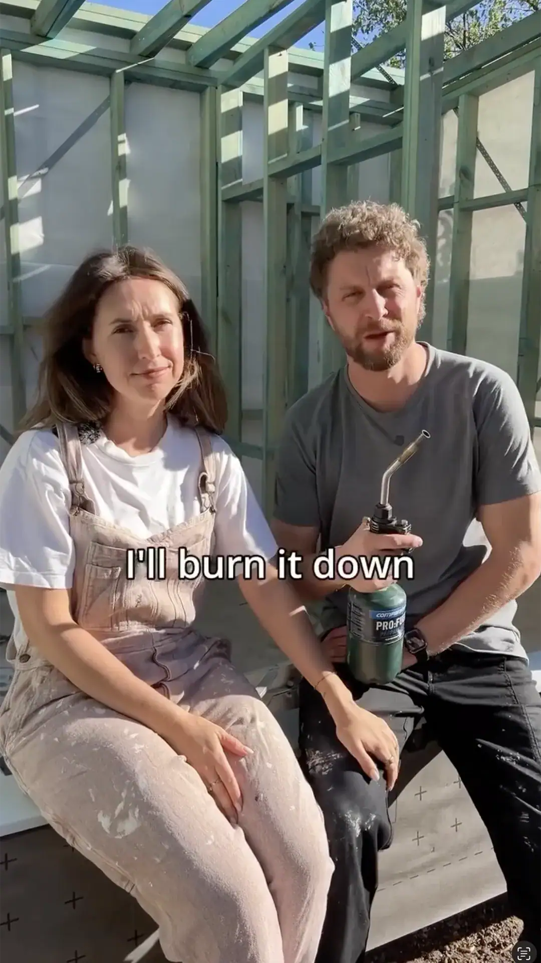 Two people sit on a construction site with a man holding a propane torch; caption reads, 'I'll burn it down'.