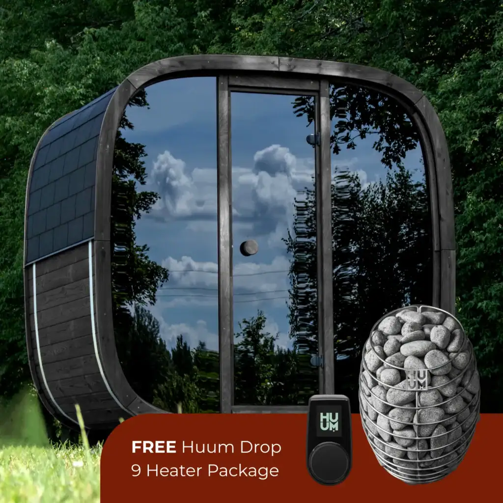 Curved outdoor sauna with glass doors reflecting clouds and trees, a stone heater set nearby, and a red promo banner offering a free Huum Drop 9 heater package.