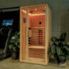Wooden sauna cabin with glass door in a gym, warm interior lighting, and two-tier benches visible.