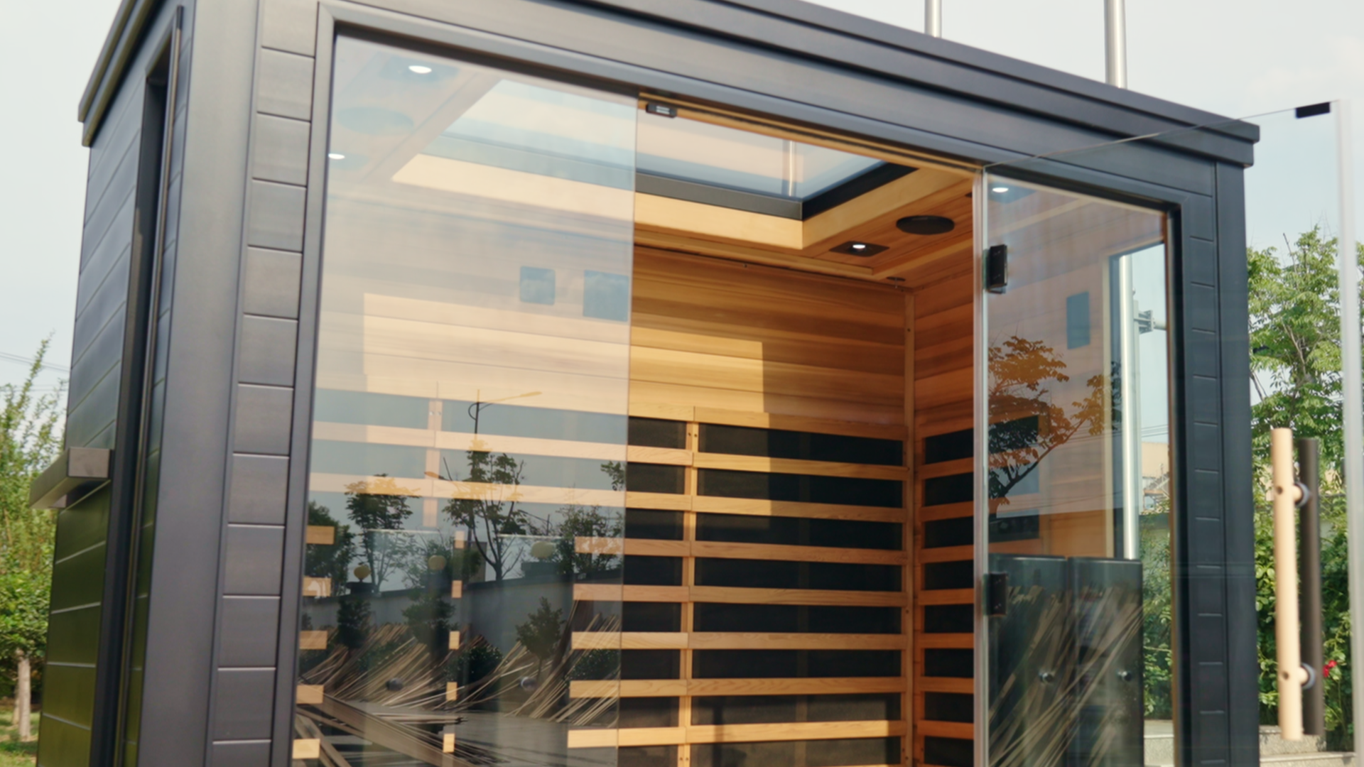 Modern glass-walled sauna cabin with wooden interior and benches, seen from outside.